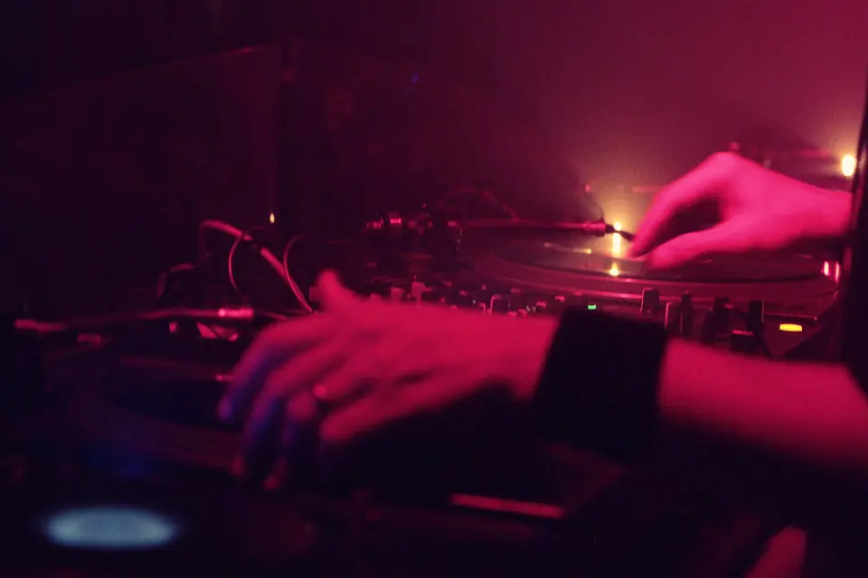 A DJ’s hands on a mixer and turntable in red club light