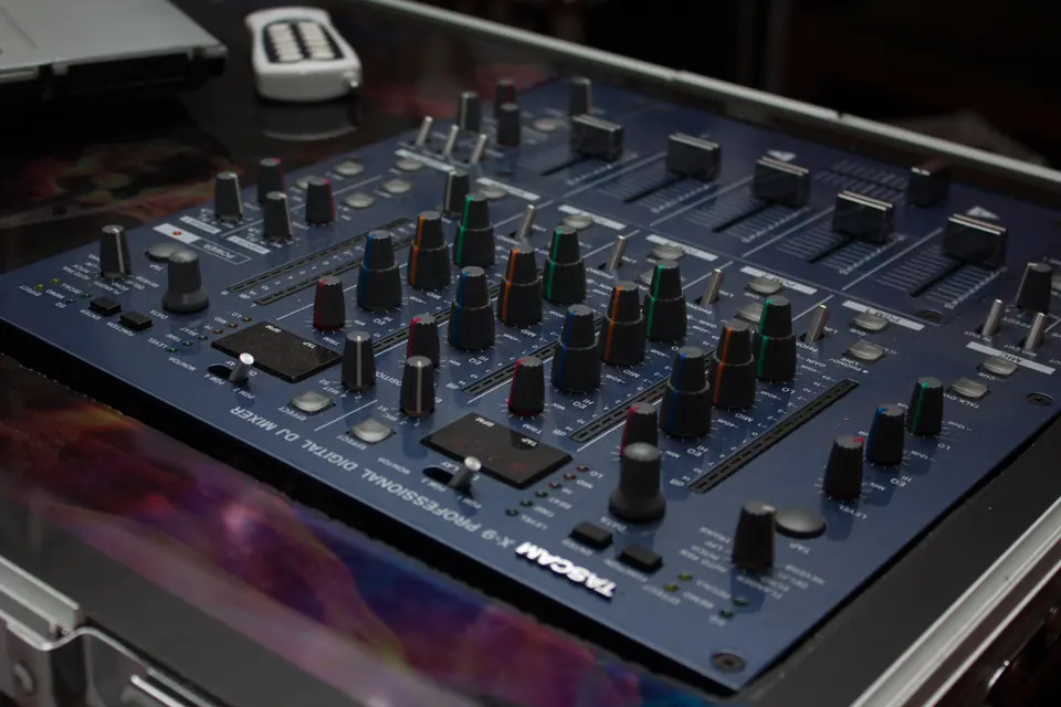 A digital DJ mixer with rows of knobs and faders on a dark table