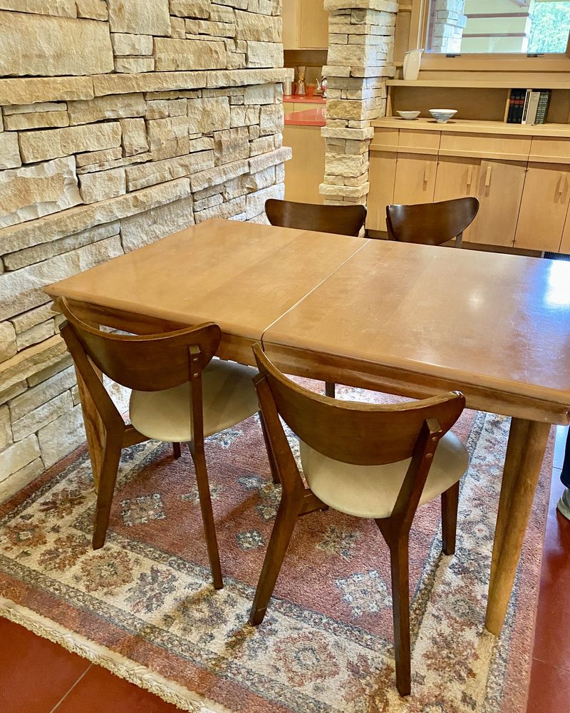 A solid timber dining table with wooden chairs beside a stone wall