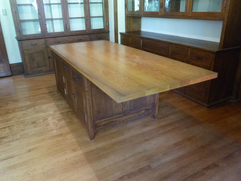 A large kitchen island with a solid wood top and timber front, glazed cabinets behind