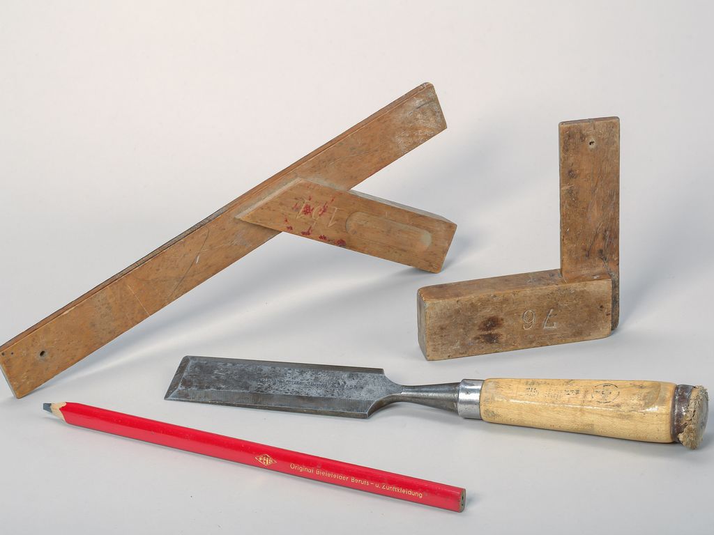 A bevel-edged chisel, two wooden try squares and a carpenter’s pencil laid out on a pale surface