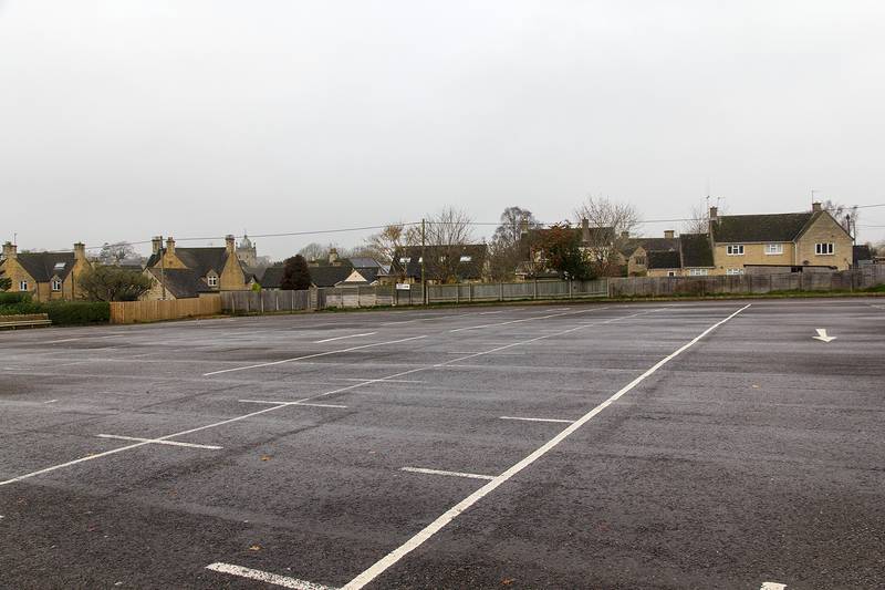 An empty car park with painted bay lines, and houses behind it.