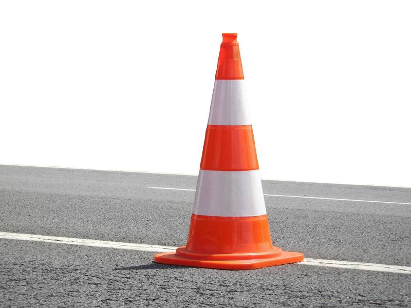 A single orange and white traffic cone standing on a road.