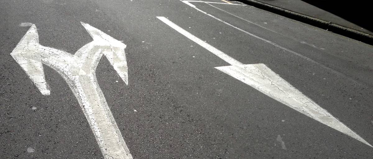 White arrows painted on tarmac, one pointing ahead and to the left, one to the right.