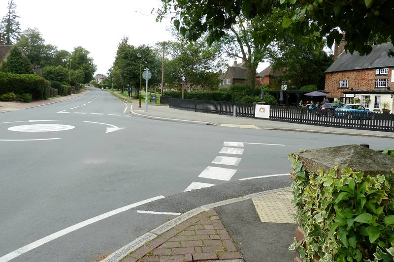 A mini-roundabout at a quiet village junction, with white road markings and a pedestrian crossing.