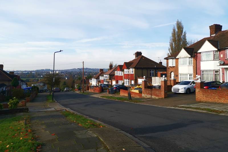 A quiet suburban road of red-brick semi-detached houses on a sunny day.