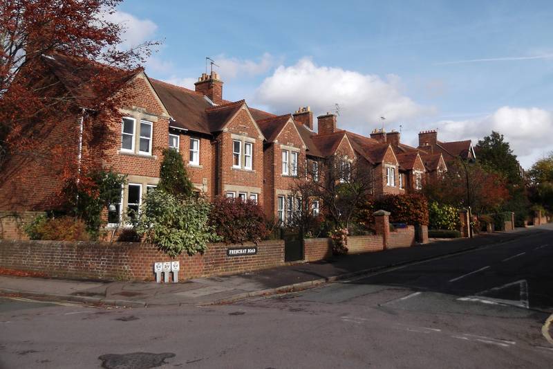 A row of red-brick terraced houses with front gardens beside an empty road.