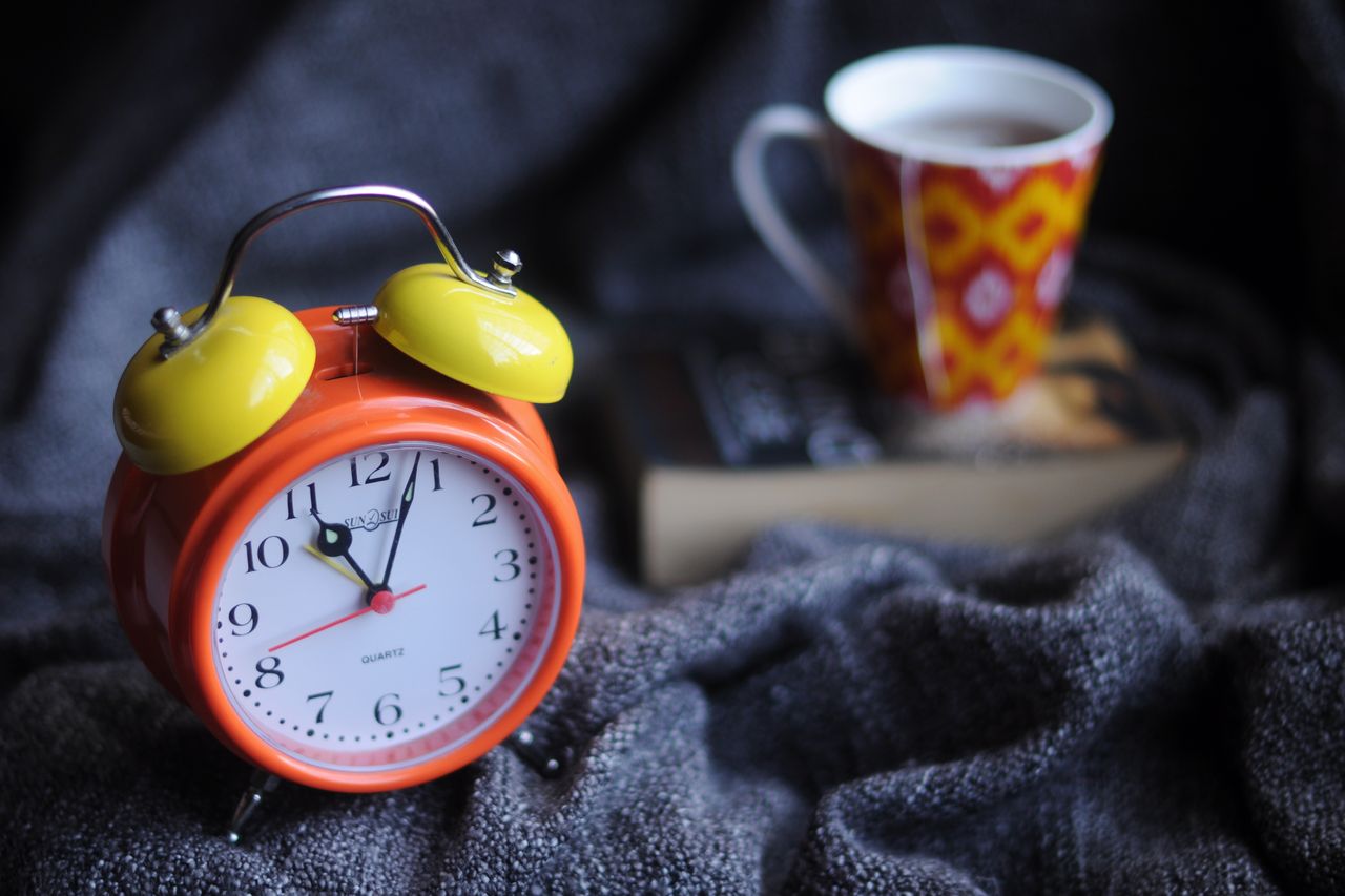 An open book, a cup of coffee and a red alarm clock on a soft blanket