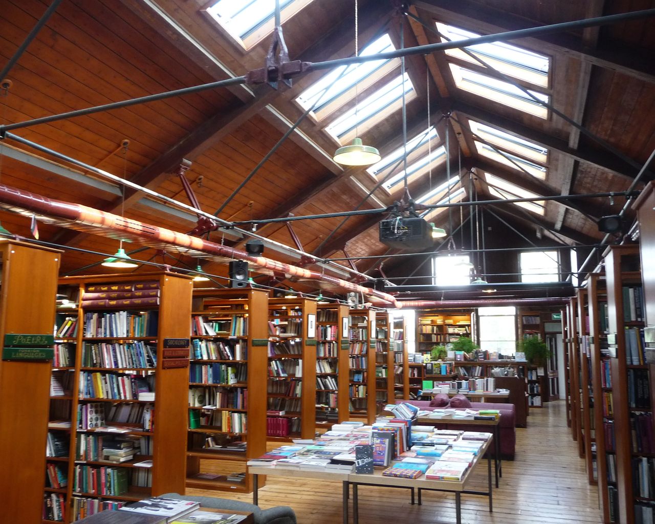 Tables and tall wooden shelves of books under a skylit roof in a large secondhand bookshop