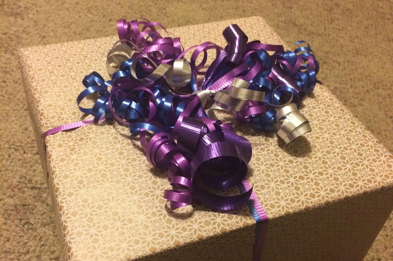 A gift box in brown paper tied with purple ribbon