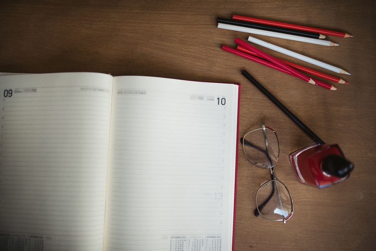 An open planner, pens and coloured pencils on a wooden desk