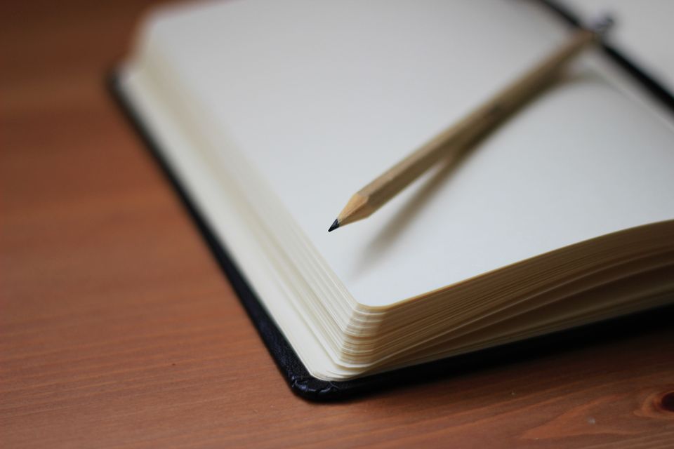 An open black notebook with a pencil on a wooden table
