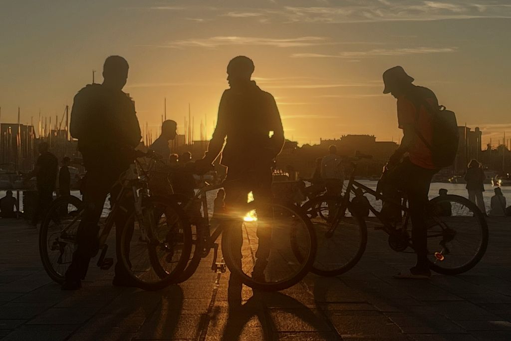 Cyclists with their bikes silhouetted against a golden sunset at the old port of Marseille