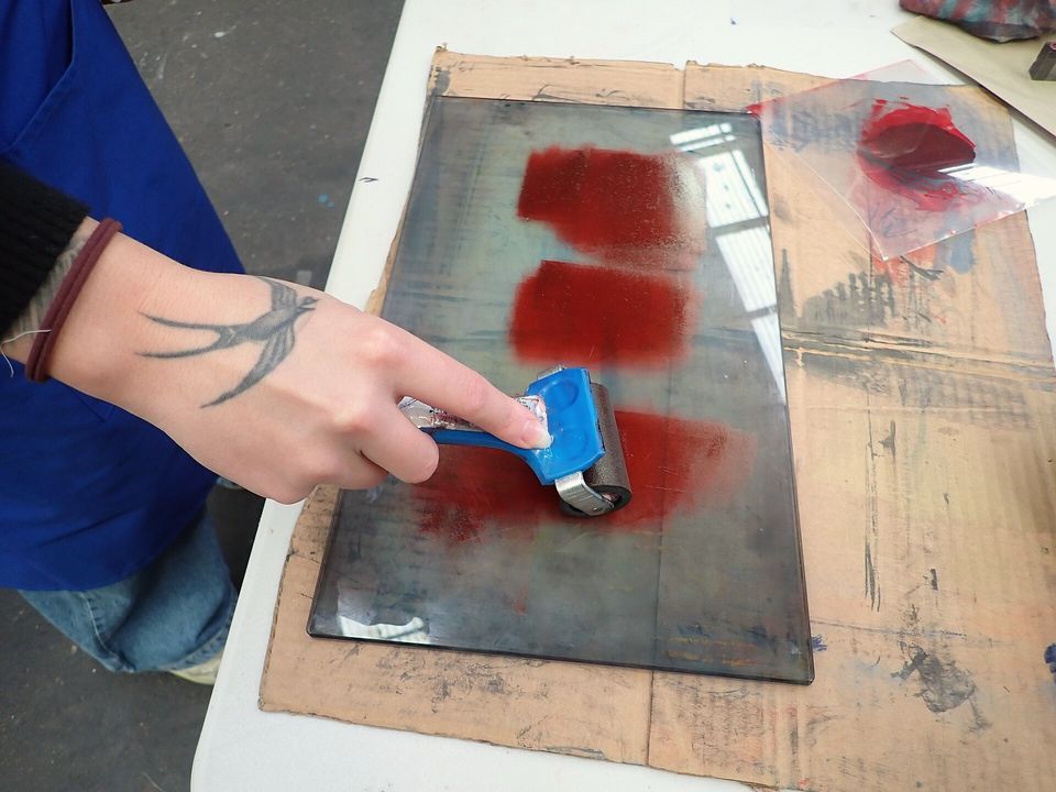 A hand rolling red ink out with a small brayer on a glass slab