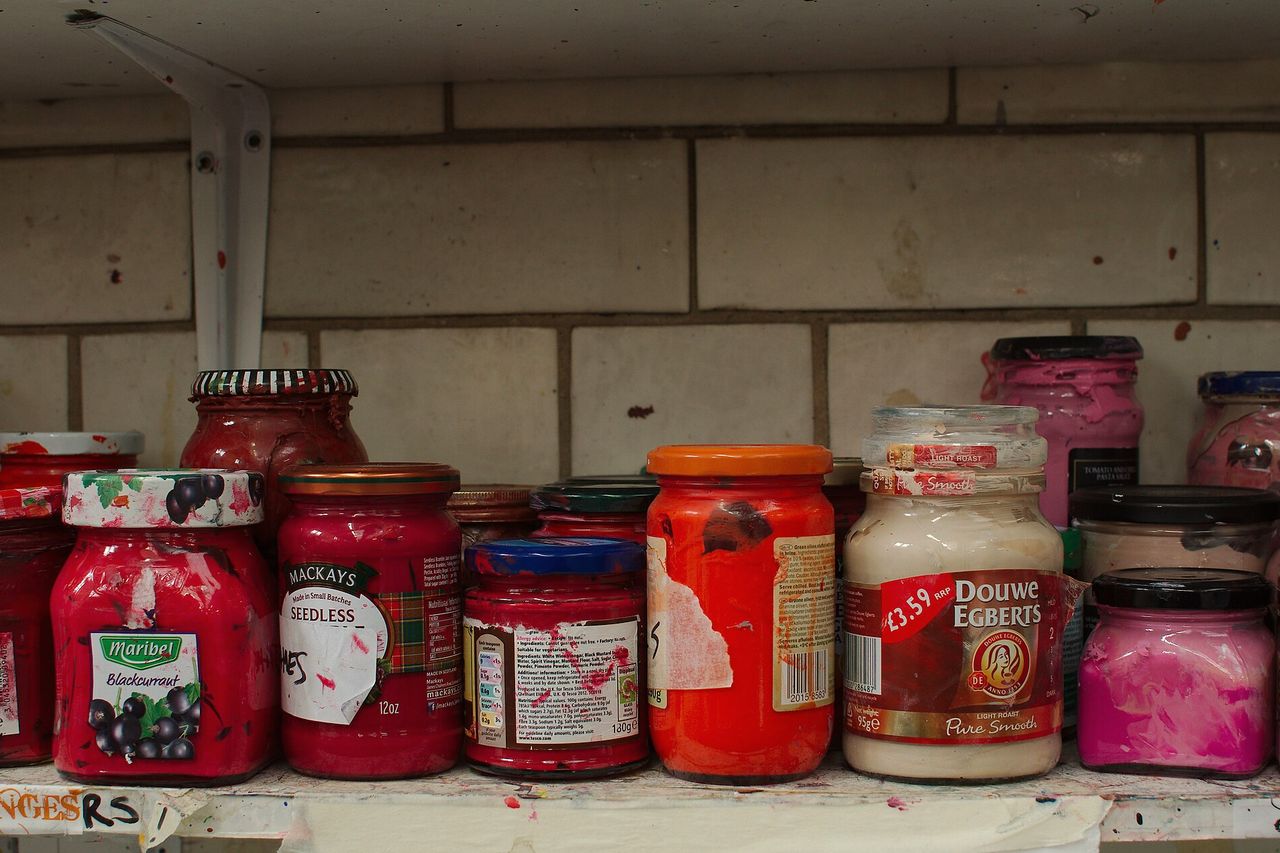 Tubs of red and pink printing ink lined up on a studio shelf