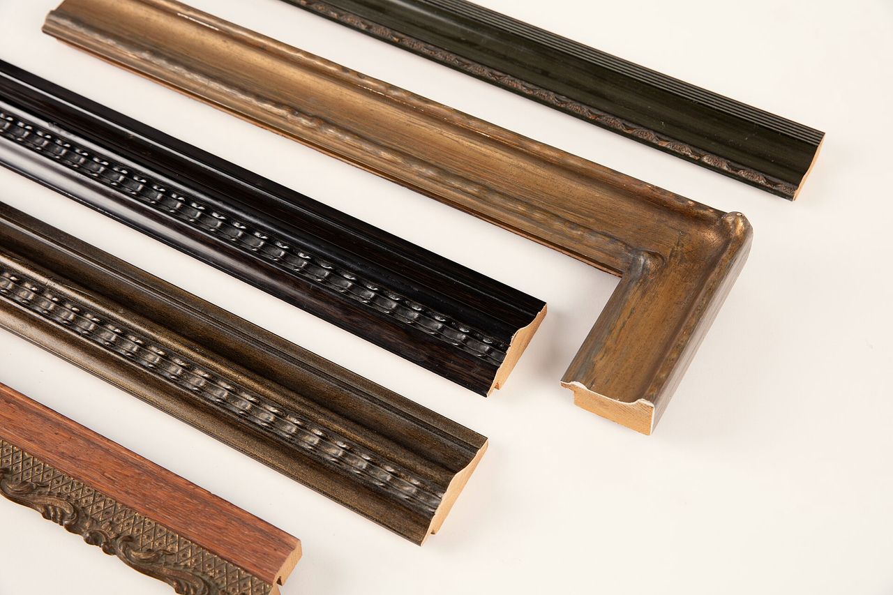 Lengths of picture-frame moulding in gilt, black and wood laid out on white