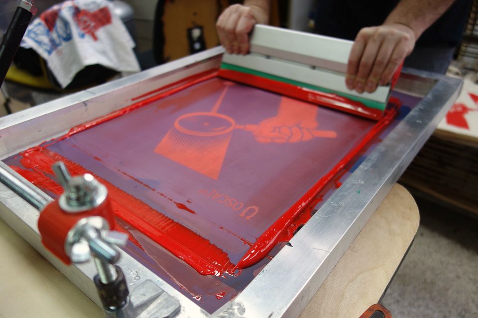 A red-coated silk screen clamped in a hinged printing frame