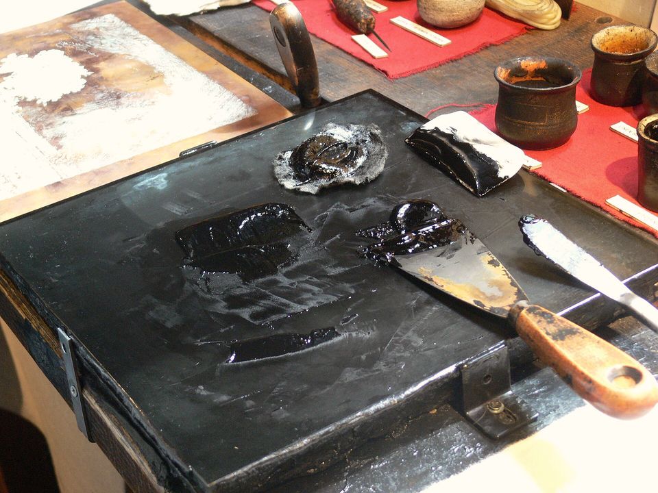 Black ink on a stone slab with palette knives and a roller beside it