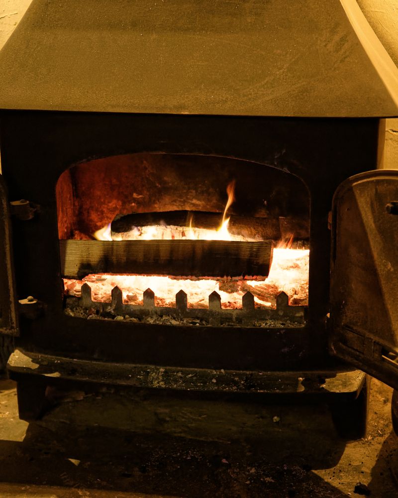 A wood-burning stove with a lit fire in a brick hearth