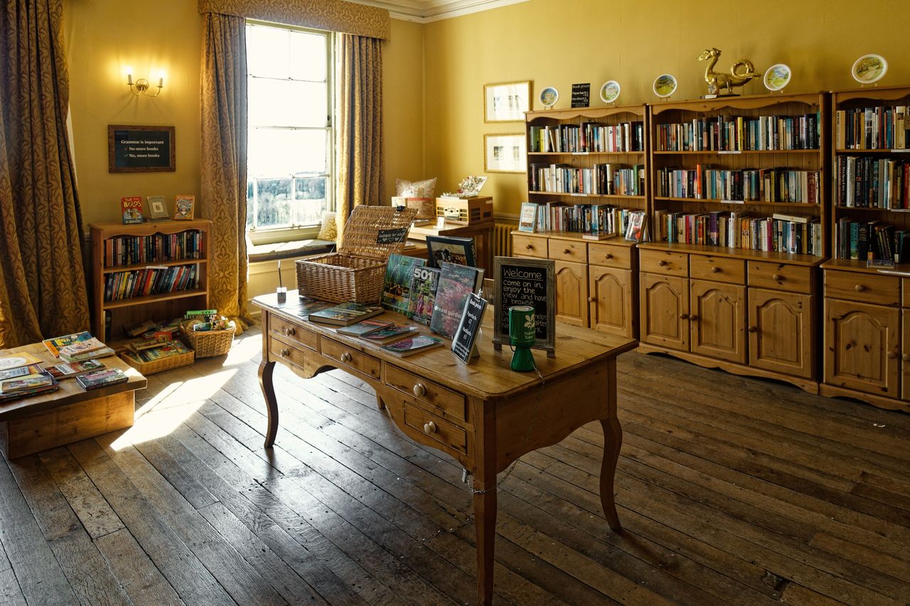 A panelled reading room with bookshelves, a writing desk and armchairs in morning light