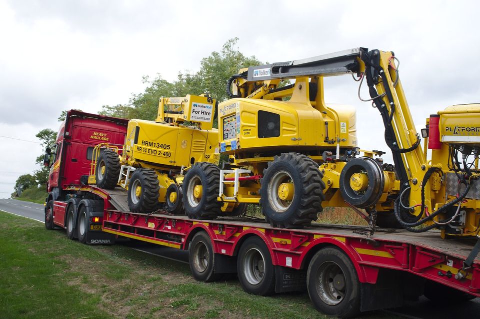 Red low loader carrying yellow construction machines