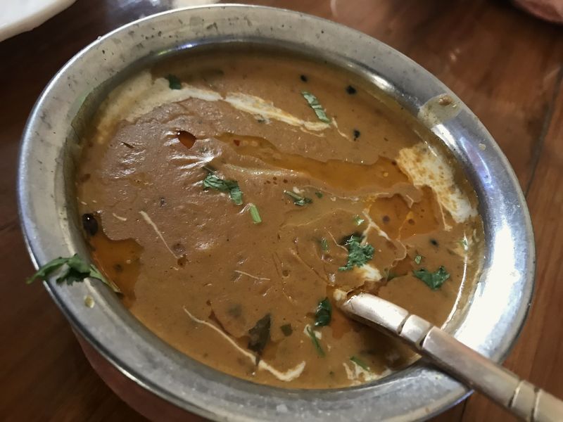 A steel bowl of dal with a spoon