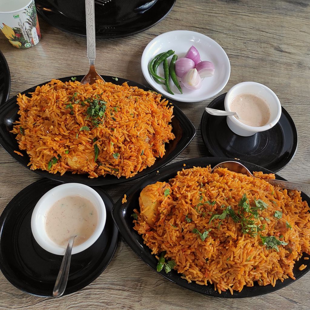 Two dark plates of chicken biryani with small cups of raita and onion on a restaurant table