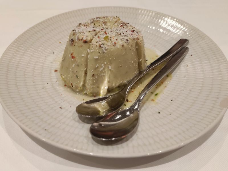 A turned-out pistachio kulfi on a white plate with two spoons