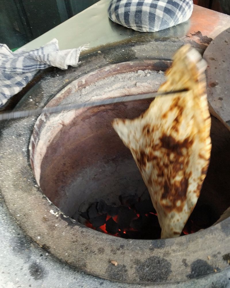 A flatbread being lifted out of a clay tandoor