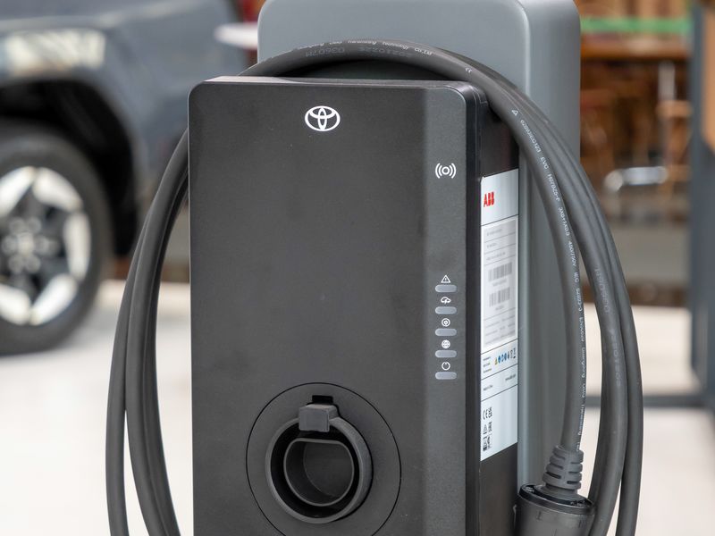 A black wallbox charger with a coiled cable mounted on a grey post
