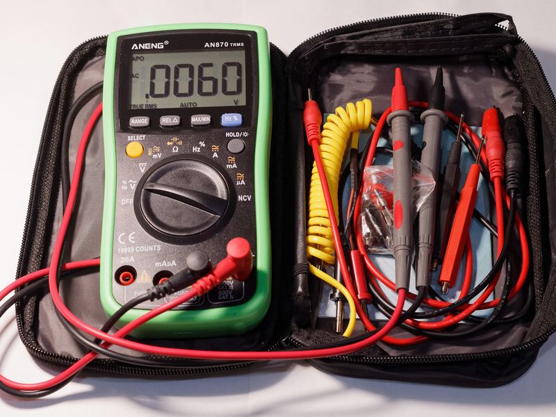 A green digital multimeter with red and black probes in an open carry case
