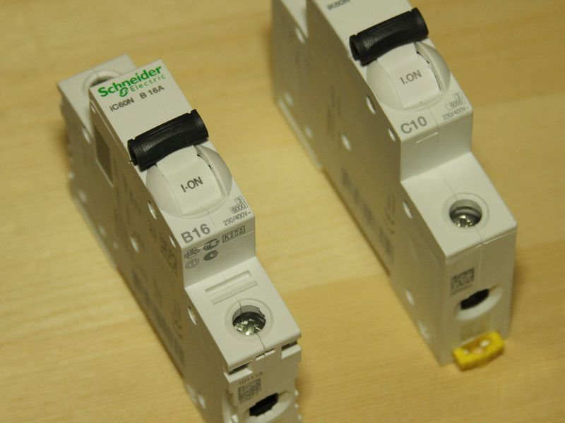 Two single-pole miniature circuit breakers standing on a wooden surface
