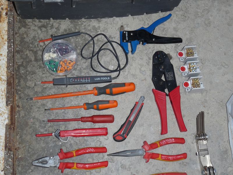 Insulated screwdrivers, pliers and a cable stripper laid out beside an open orange parts case