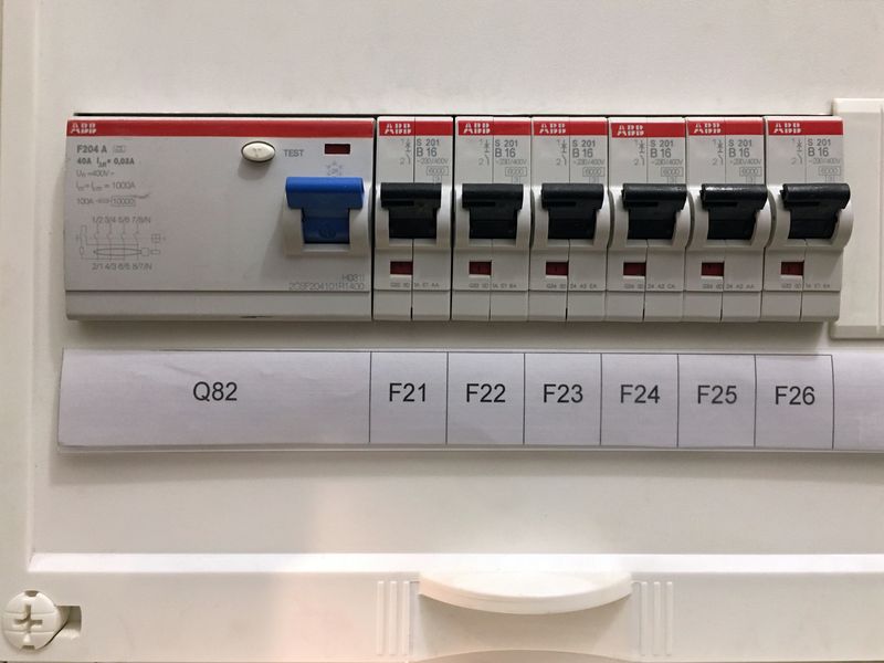 A row of grey circuit breakers with printed circuit labels in a modern board