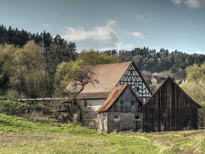 A timber-framed mill house with a red roof beside a wooden barn