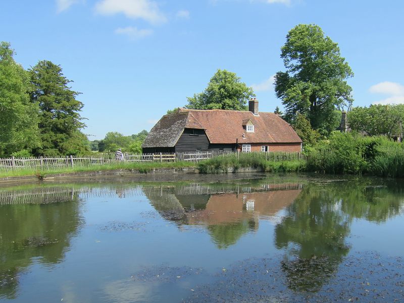 A red-roofed mill house reflected in a still mill pond