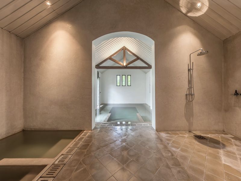 A small indoor plunge pool and an open shower in a white stone room
