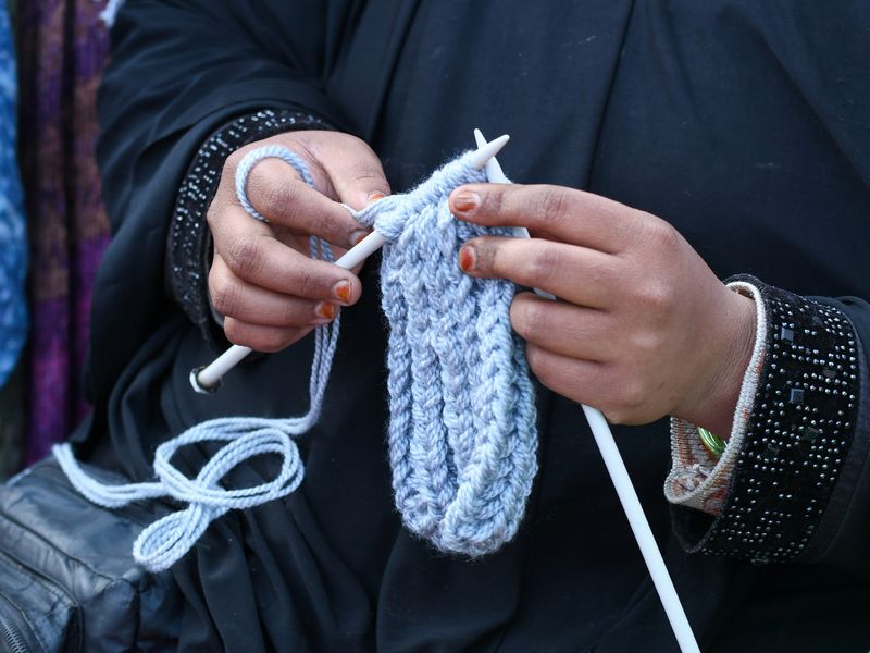 Hands knitting pale blue yarn on long straight needles