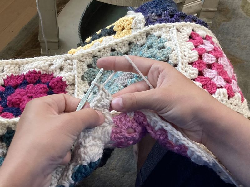 Hands crocheting a granny-square blanket