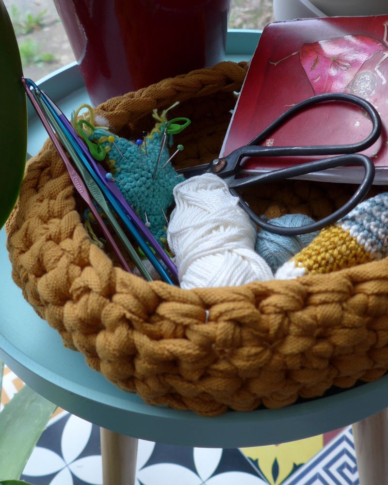 A chunky crocheted basket holding yarn, scissors and a notebook