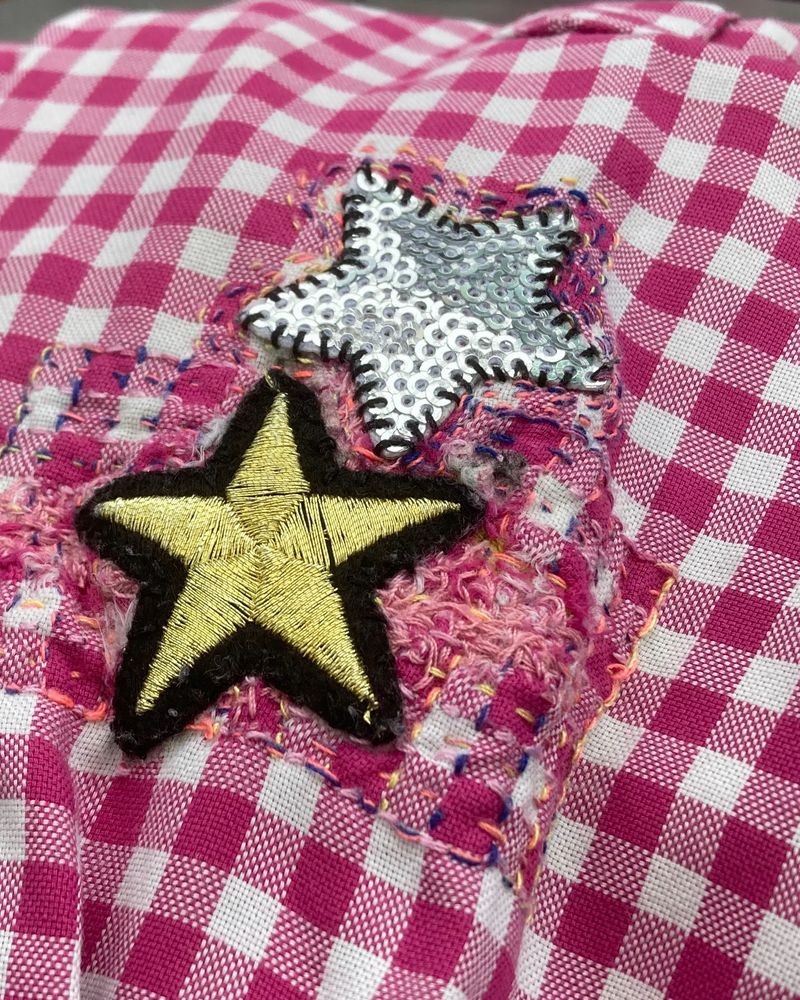 A visibly mended gingham shirt with star patches and embroidery