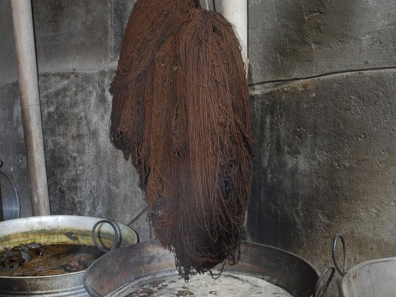 A brown skein of wool hanging over a dye pot