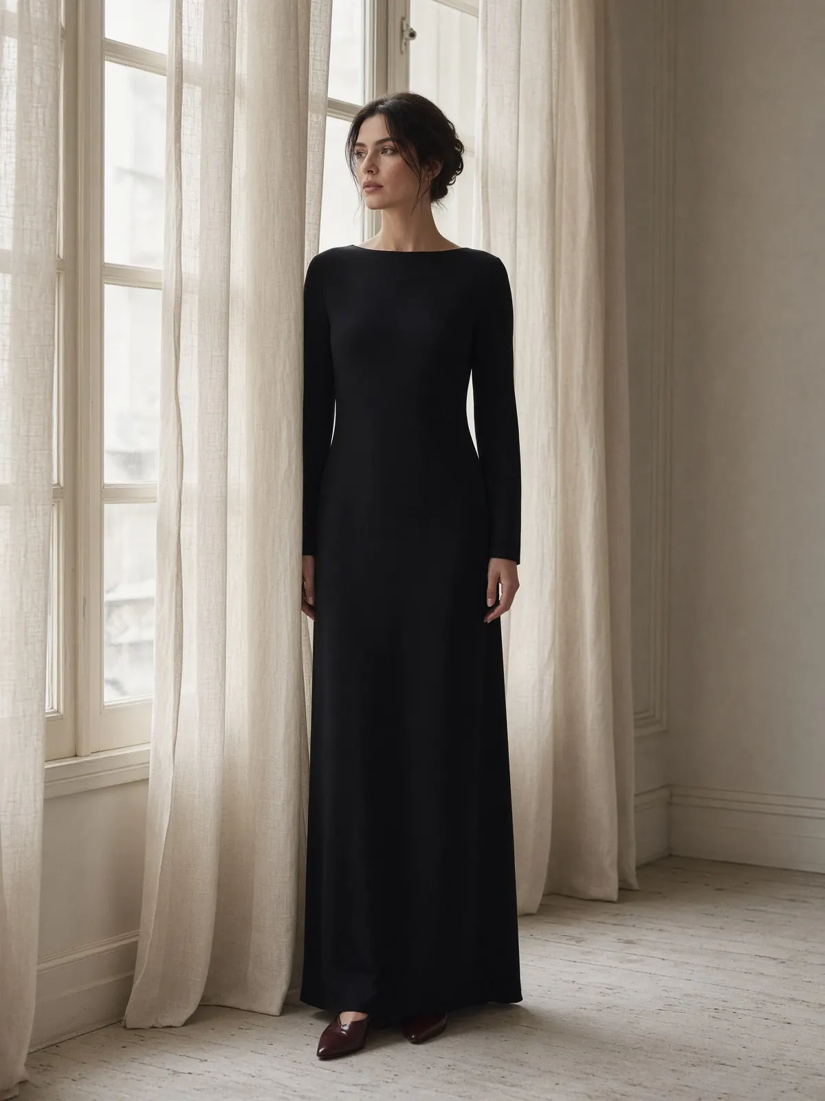 Ink wool-crepe column dress with a boat neck, worn beside tall windows.