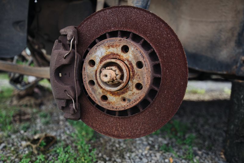A rusty brake disc and caliper on a car with its wheel removed