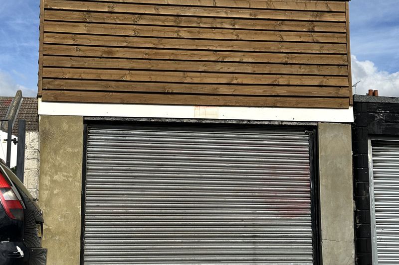 A timber-clad lock-up garage with a closed grey roller door