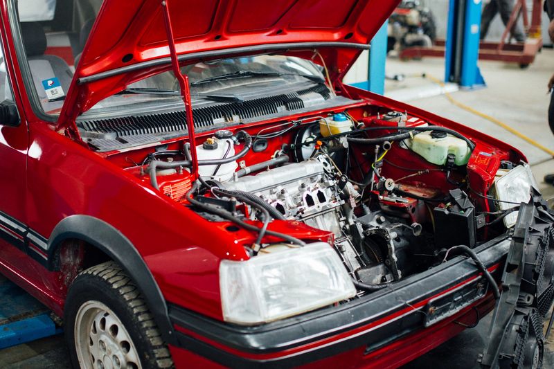 A red Peugeot 205 convertible with its bonnet open in a workshop