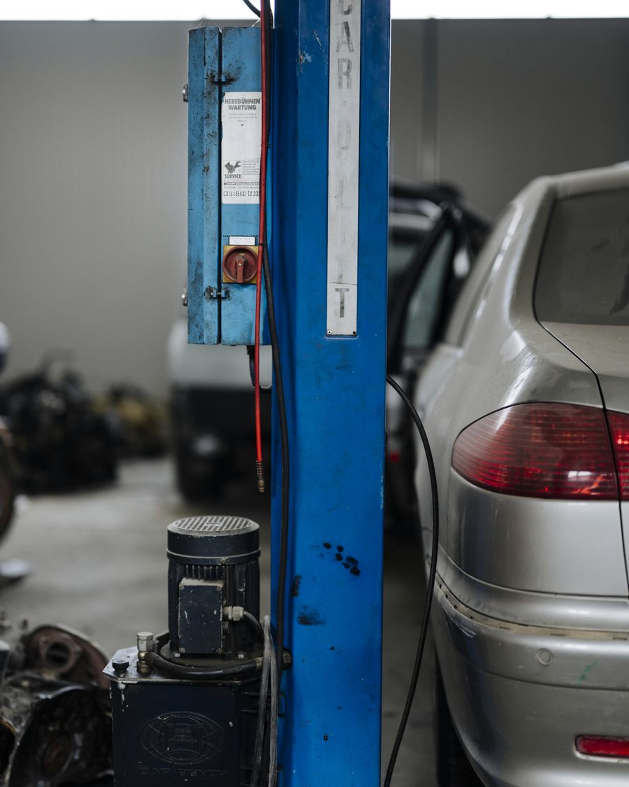 A blue two-post lift beside a silver car in a workshop, with tools and parts on the floor