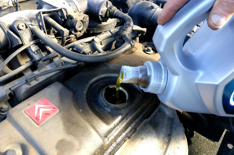 Engine oil being poured from a blue bottle into an engine filler neck