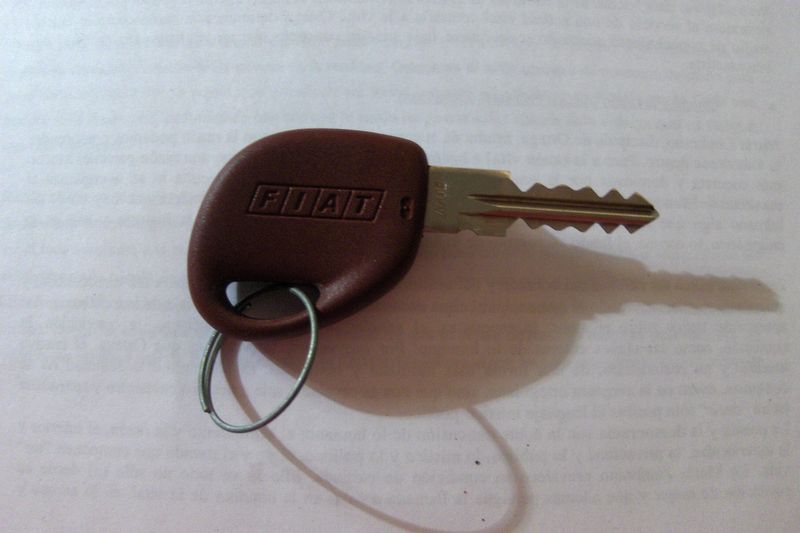 A car key with a brown plastic head and a key ring on a white surface