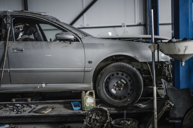 A silver car raised on a lift with a front wheel off and tools on the floor below